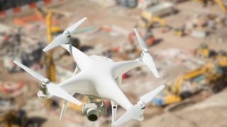 Unmanned Aircraft System (UAV) Quadcopter Drone In The Air Over Construction Site.