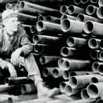 Image from the 1920's of a stack of grooved pipe and a workman taking a break - Victaulic