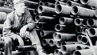 Image from the 1920's of a stack of grooved pipe and a workman taking a break - Victaulic