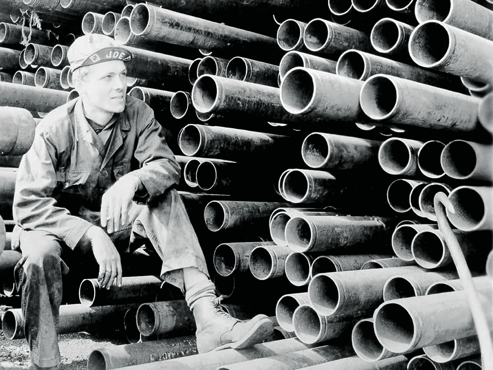 Image from the 1920's of a stack of grooved pipe and a workman taking a break - Victaulic