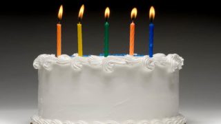 White birthday cake profile on graident background with five colorful lit candles