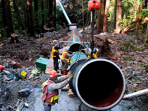 Section of penstock pipe held in air; installers in background.
