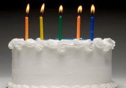 White birthday cake profile on graident background with five colorful lit candles
